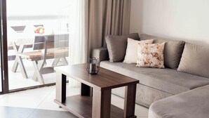 A modern living room with a grey sofa, a wooden coffee table, and a glass door leading to an outdoor seating area. - Step to Kotor bay Stoliv (Donji Stoliv)