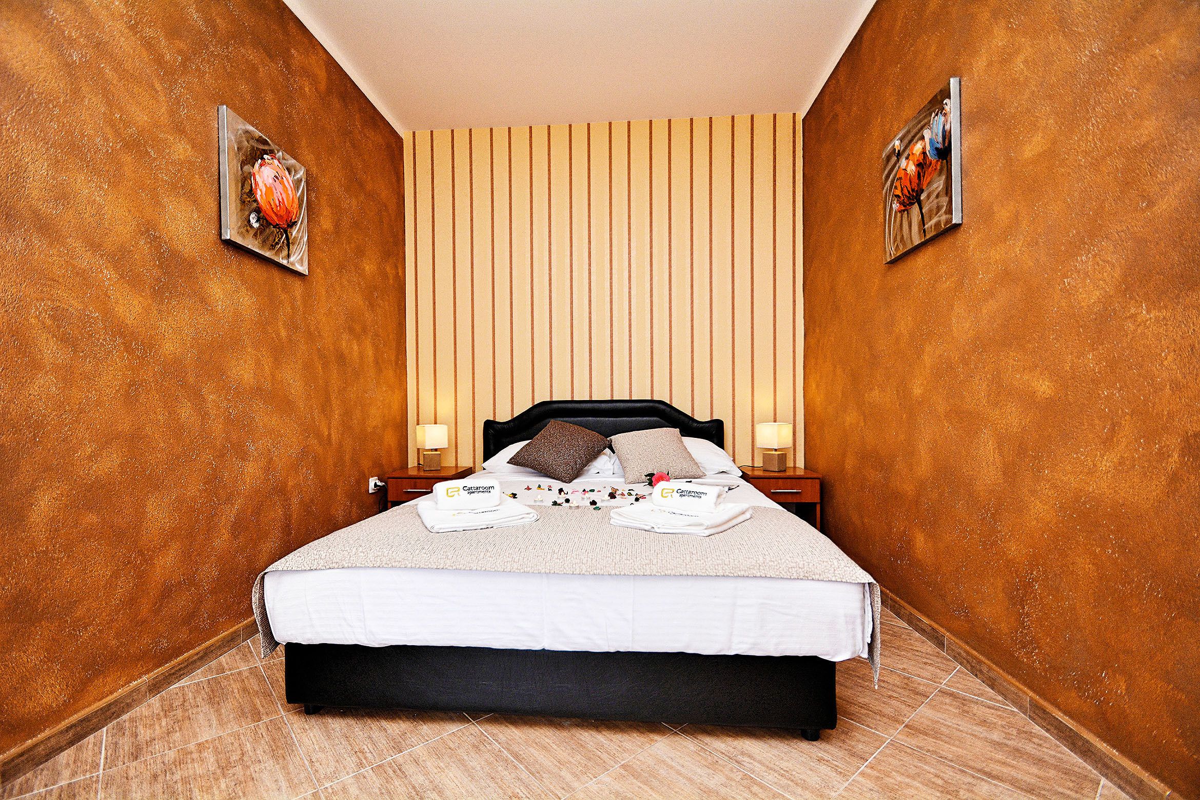 Una cama bien hecha con toallas, cabecera y una pared con líneas verticales.