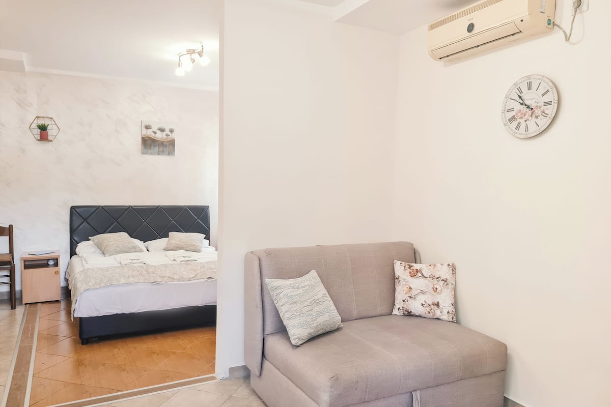 A bedroom with a bed, a sofa, a wall clock, and a ceiling fan.
