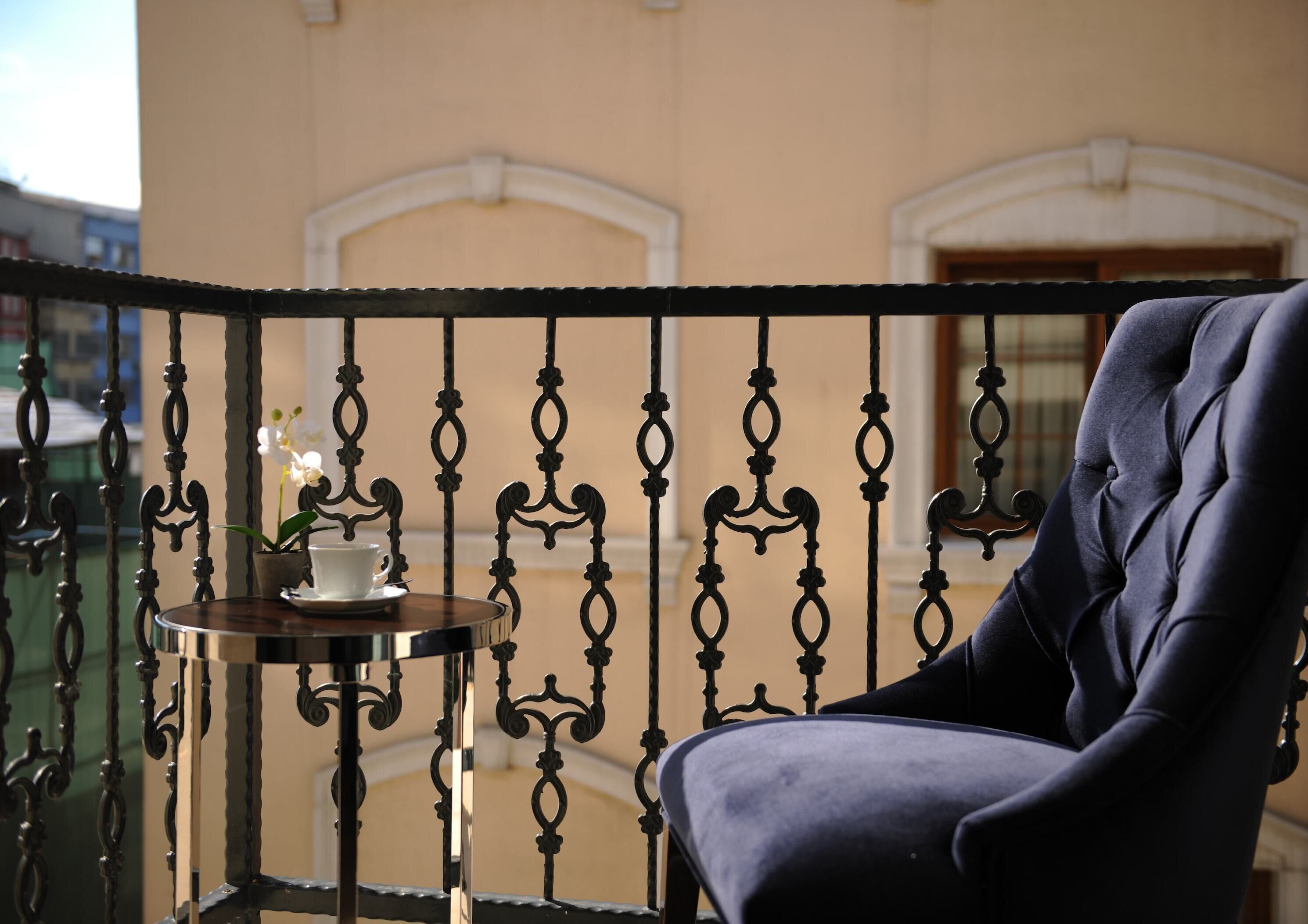 A balcony with a wrought iron railing, a potted orchid, a white cup, and a plush armchair.