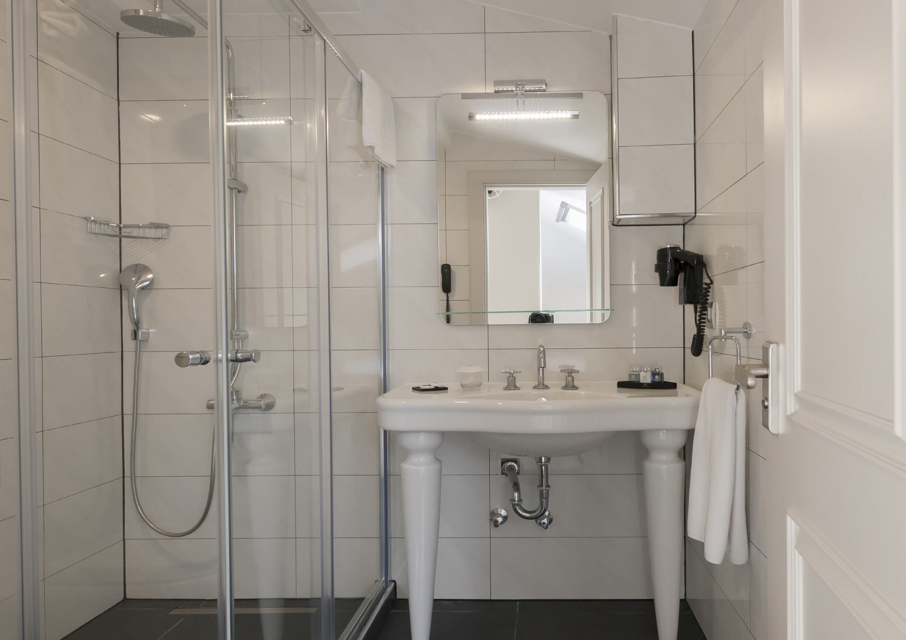A modern bathroom with a glass-enclosed shower, a white sink with a mirror above, and a towel rack.