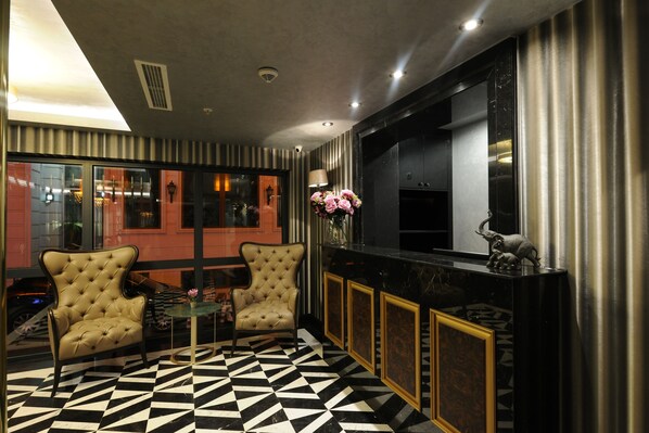 A modern interior with a black and white checkered floor, two upholstered armchairs, a small round table, and a bar area with a mirror and decorative items.