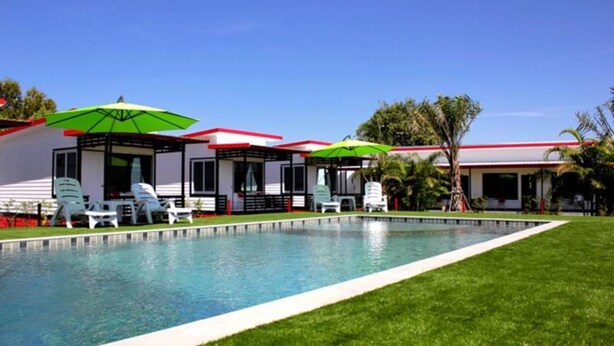 A pool area with lounge chairs and umbrellas, surrounded by a well-maintained lawn and a building with a red roof. - Cape Go Resort (Tha Mai)