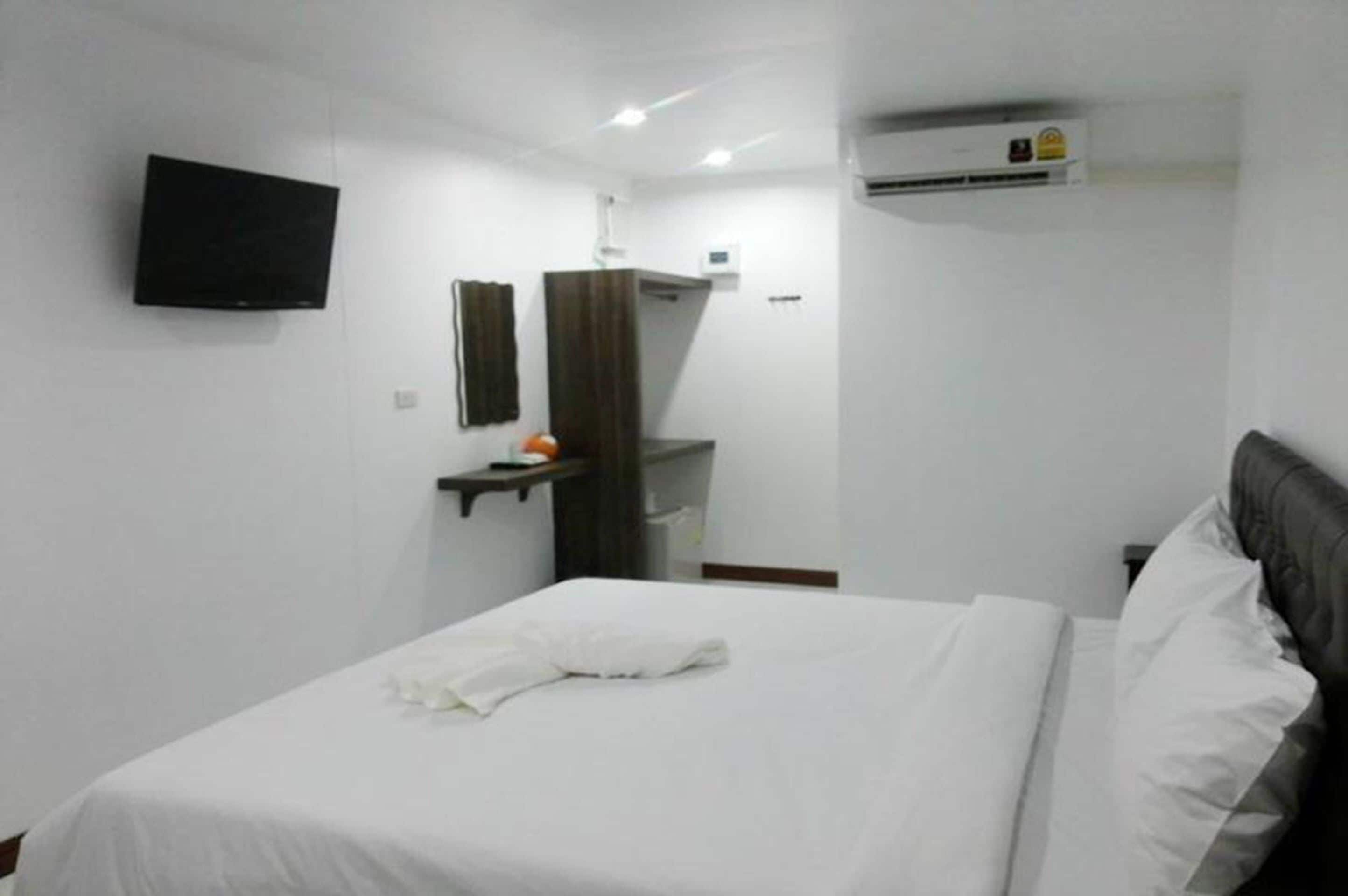 A hotel room with a bed, a flat-screen TV mounted on the wall, a mirror, and an air conditioning unit.