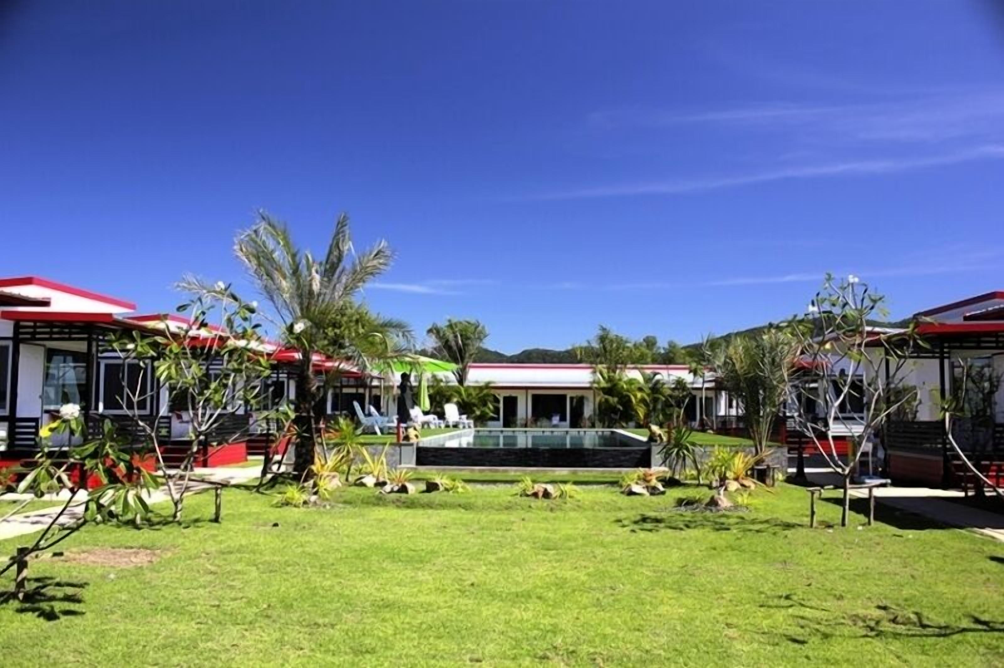 A hotel with multiple red-roofed buildings, a central pool area, and well-maintained tropical landscaping.