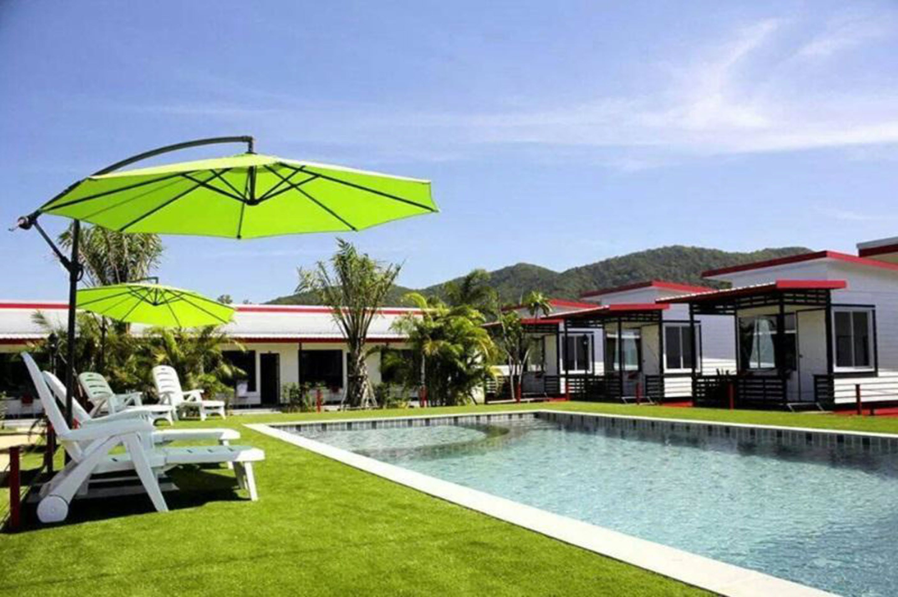 A swimming pool with lounge chairs and umbrellas, surrounded by a building with a red roof and white walls.