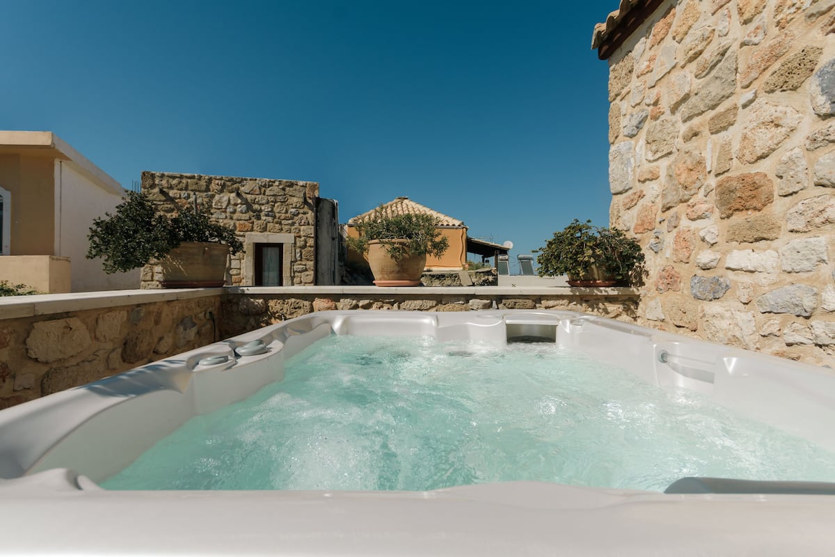 A hot tub with a stone wall and potted plants in the background.