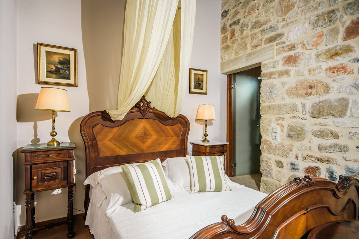 A bedroom with a wooden headboard, two bedside tables with lamps, a bed with striped pillows, and a stone wall.