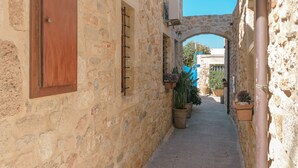A narrow stone alleyway with a wooden door and potted plants. - Casa Di Veneto (Hersonissos)
