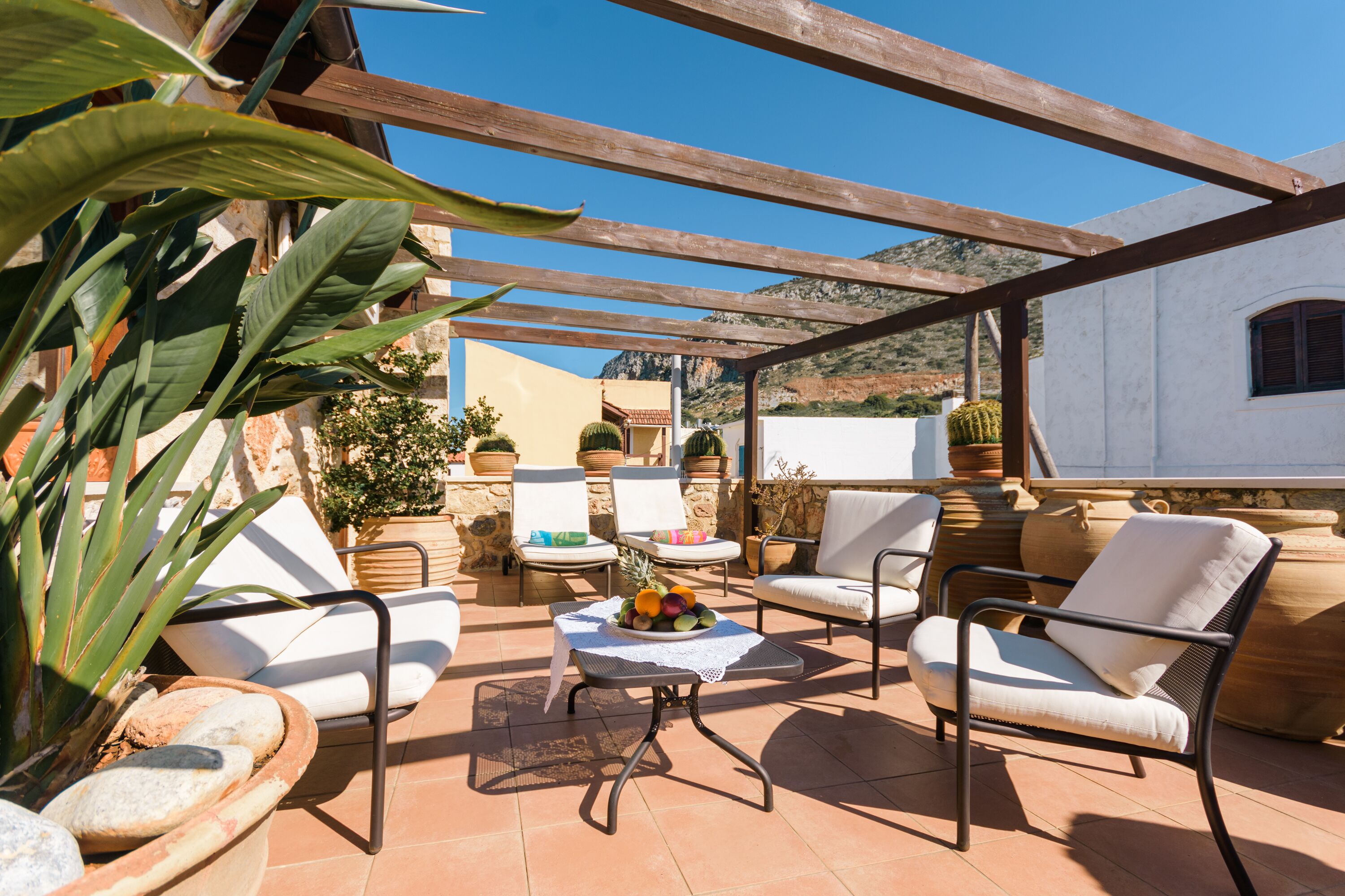Eine Terrassenausstattung mit weißen Sitzmöbeln, einem Tisch mit Früchten und Blumentöpfen.