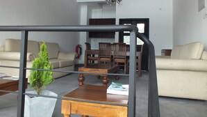 Een woonkamer met een bank, een houten eettafel en stoelen. Op de tafel staat een kleine plant in pot en een boek.