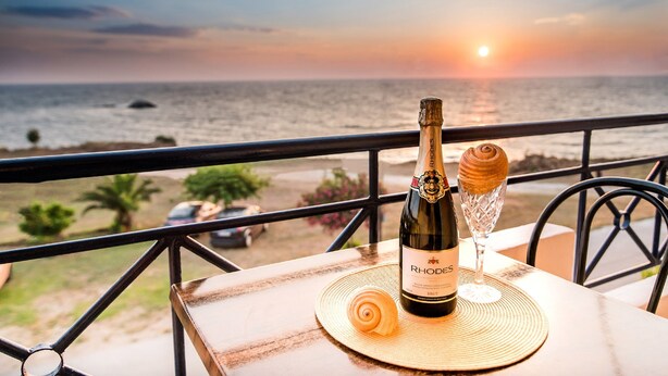 Une bouteille de vin et un verre sur une table, avec vue sur l’océan au coucher du soleil.