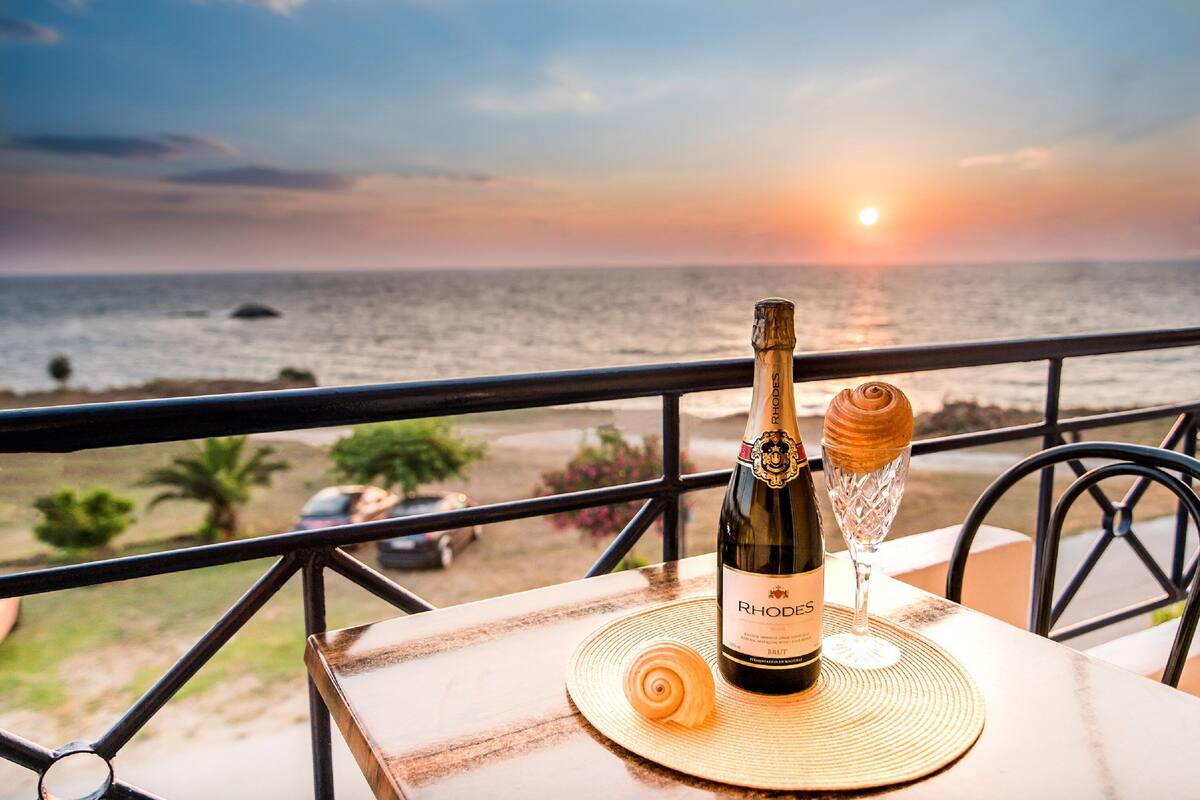A bottle of wine and a glass on a table with a view of the ocean at sunset.