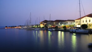 Un port de plaisance avec des bateaux amarrés, des bâtiments abritant des boutiques et une étendue d’eau calme qui reflète les lumières.