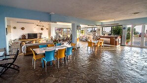Un vaste espace à manger doté d’un sol en pierre, une cuisine à l’arrière-plan et une vue sur l’extérieur grâce à de grandes portes coulissantes.
