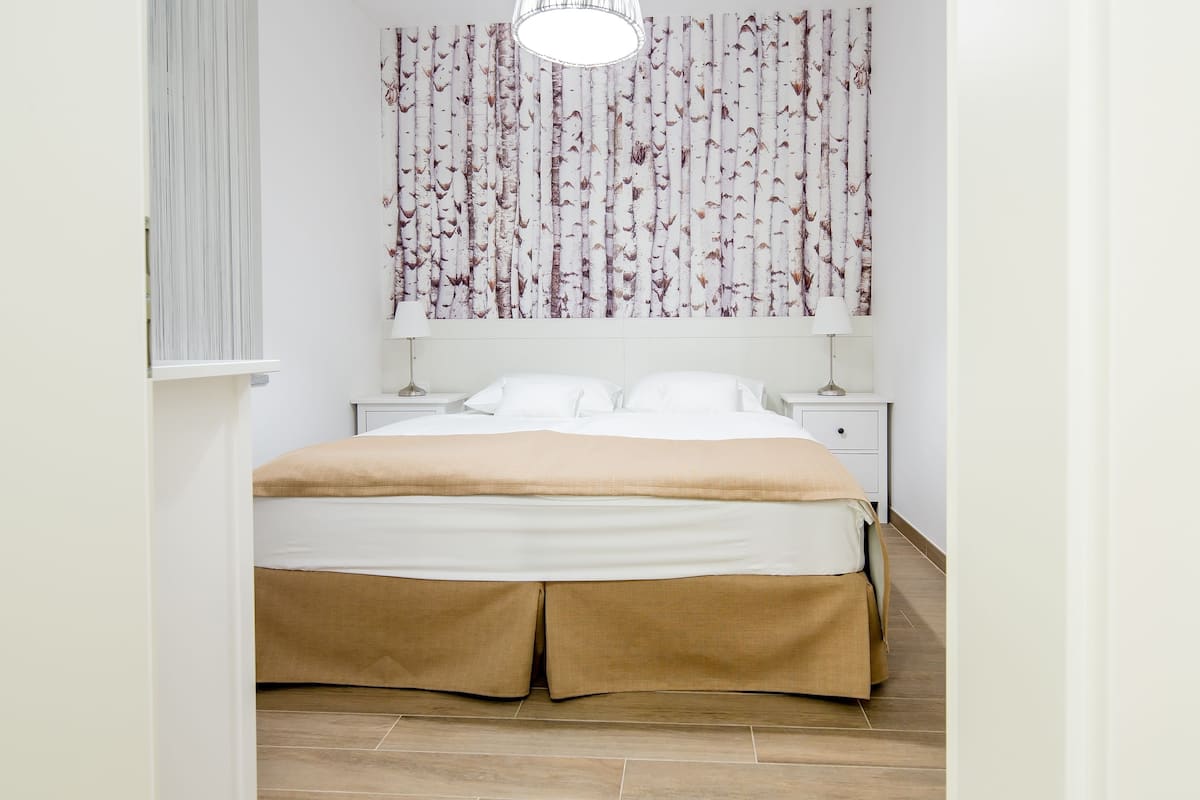 Une chambre à coucher avec un lit, des rideaux blancs, une lampe fixée au mur et une table de chevet.