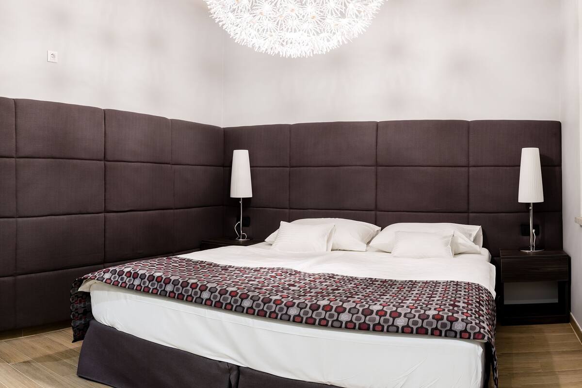 Une chambre moderne avec un grand lit, deux tables de chevet, un panneau décoratif mural et un luminaire suspendu.