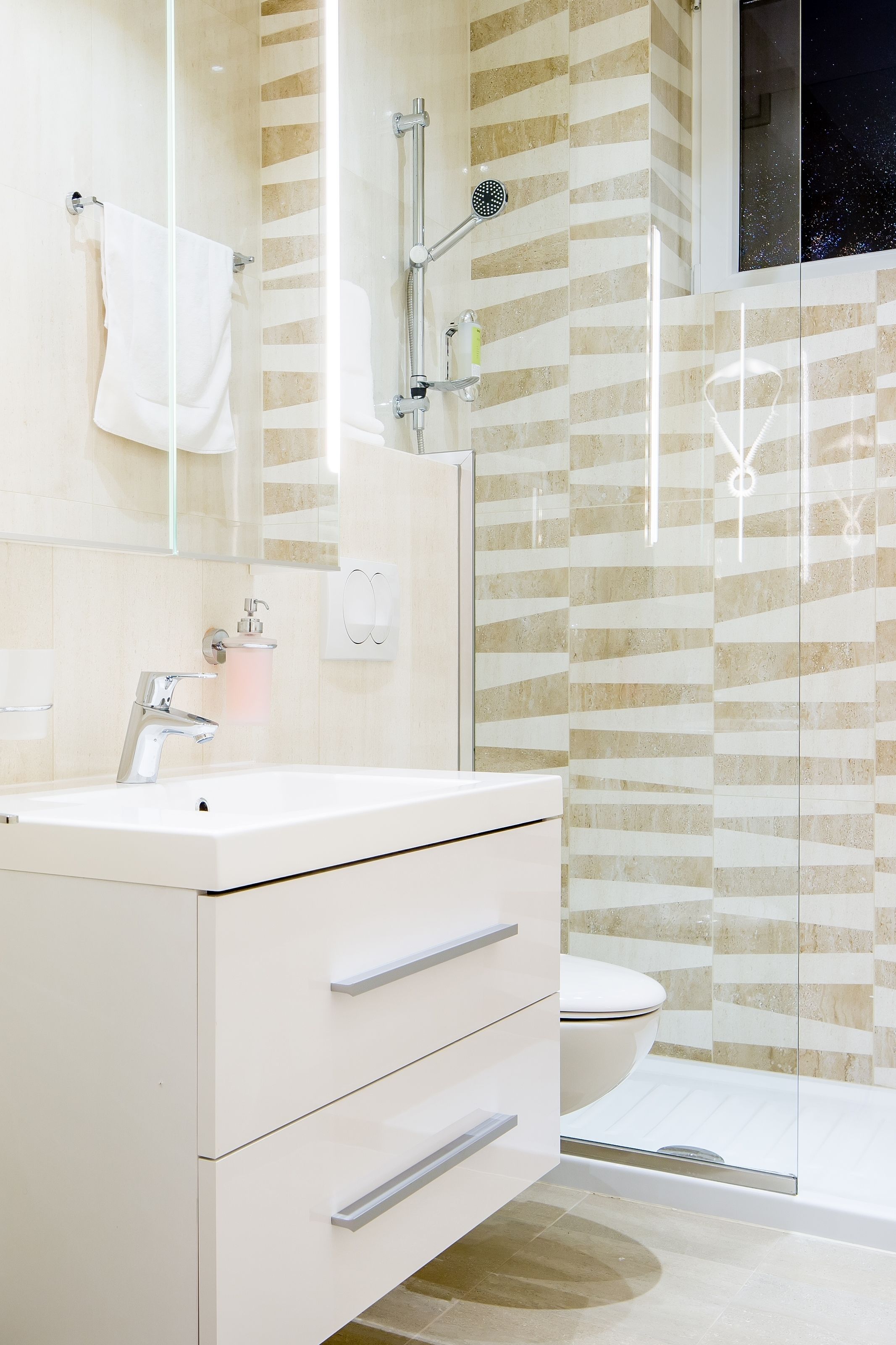 Een moderne badkamer met een witte wastafel, een glazen douchecabine en een wand met een patroon.