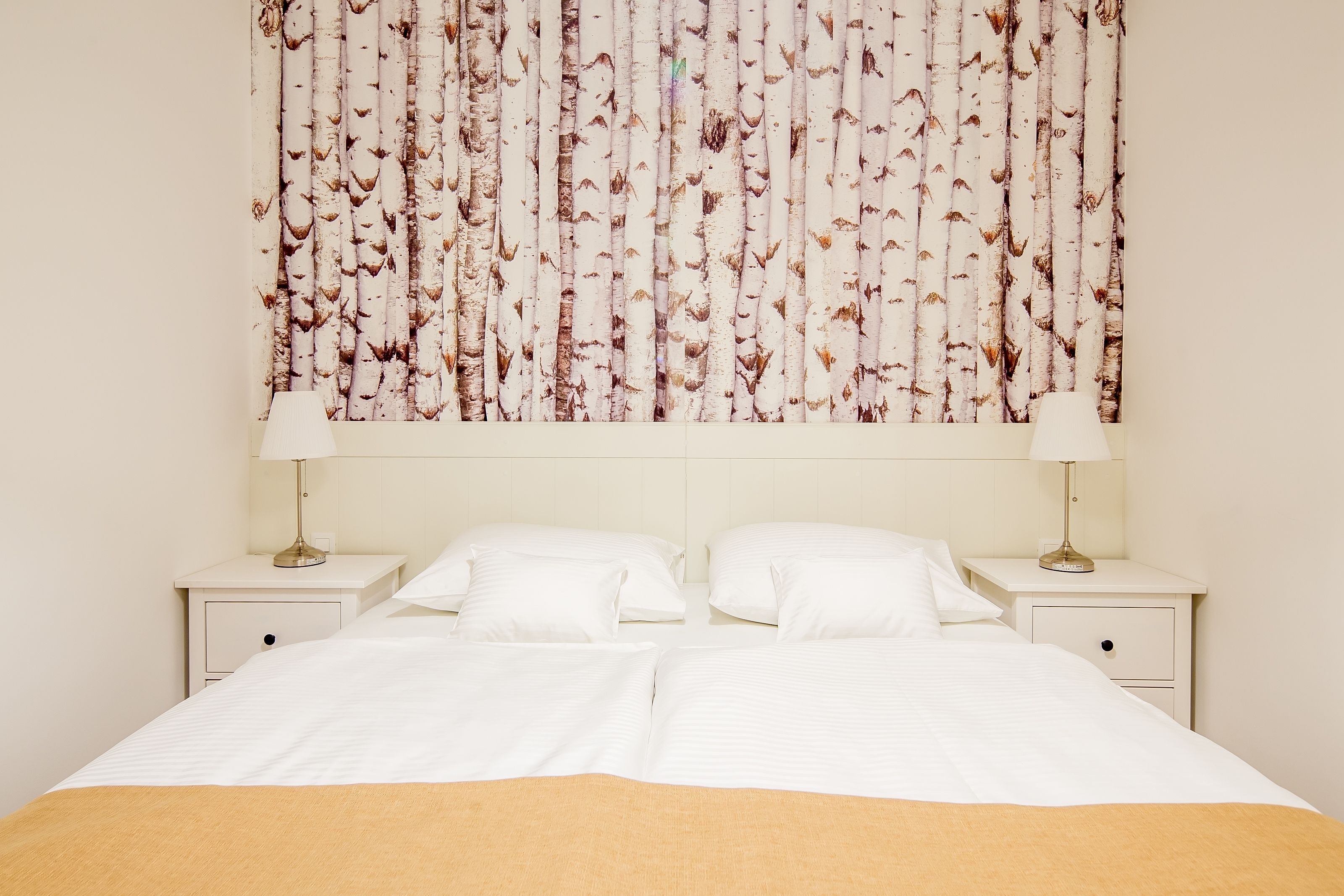 Una camera d'albergo con un letto grande, due comodini con lampade e una parete decorata con un motivo a betulla.