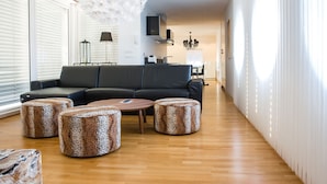 Una sala de estar moderna con un sofá seccional negro, tres otomanas con estampado de leopardo, una mesa de centro de madera y una araña blanca.