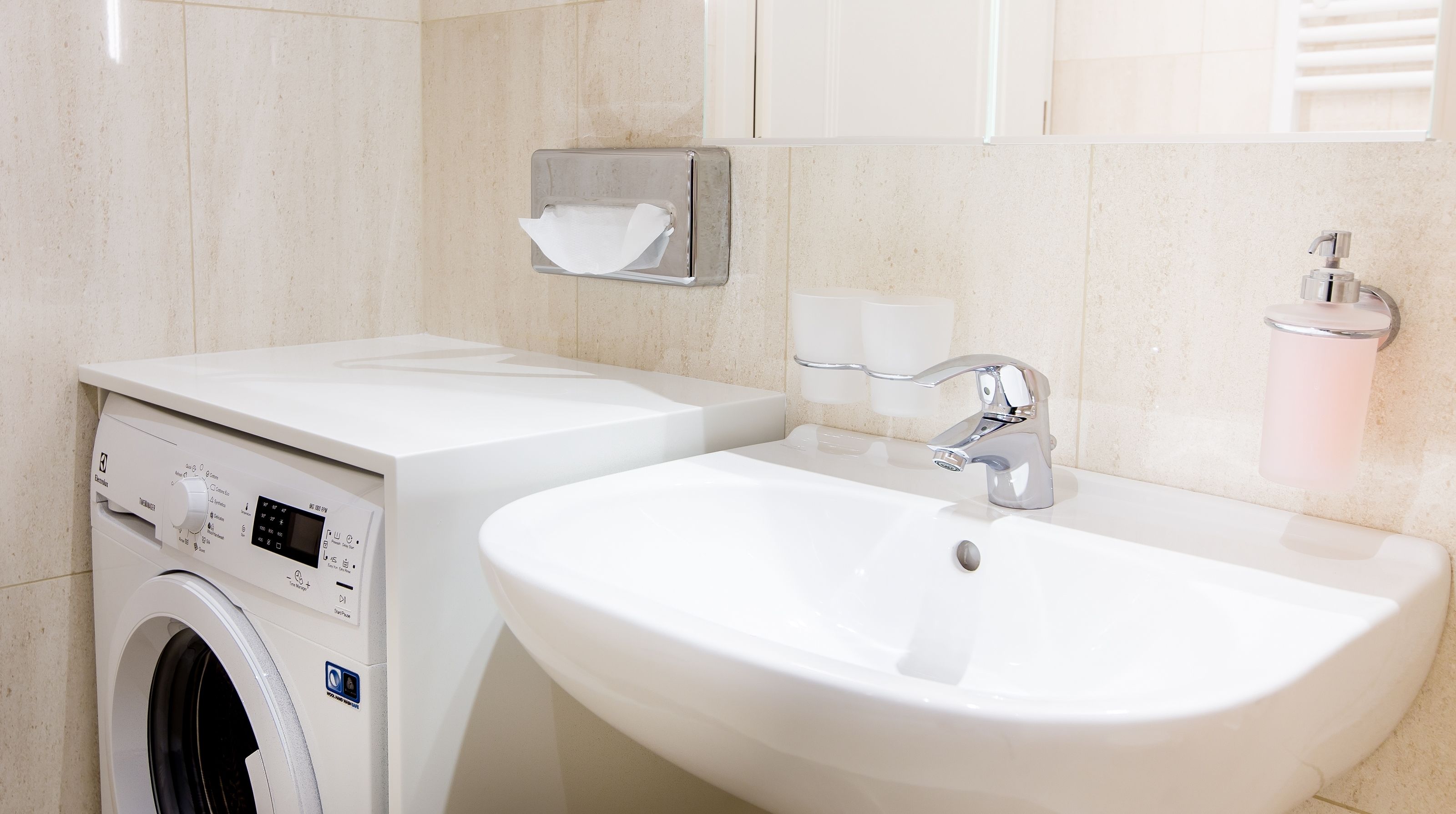 A modern bathroom with a built-in washing machine, a sink, and a toilet paper holder.