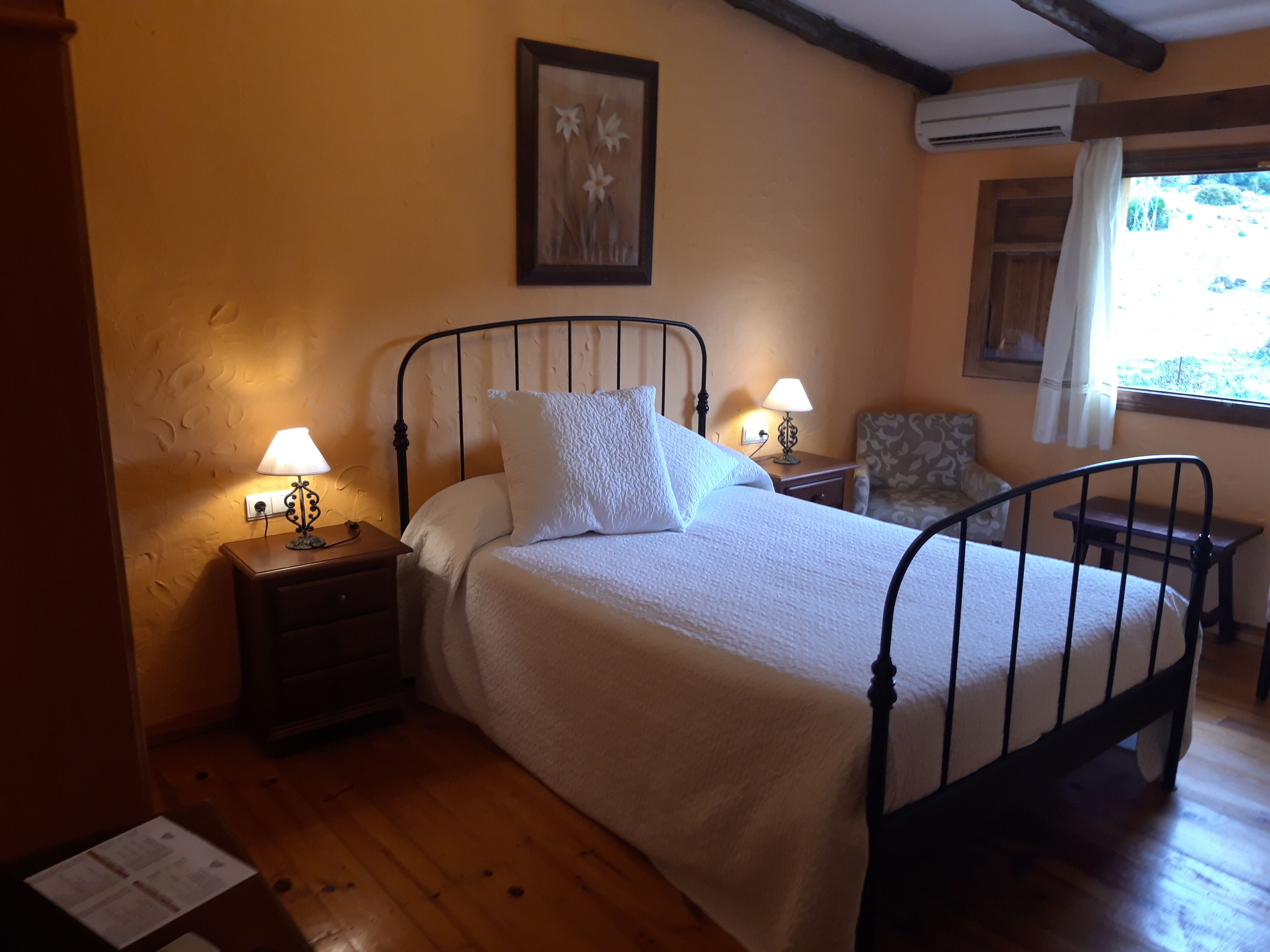 A bedroom with a bed, two bedside tables with lamps, a chair, and an air conditioning unit.