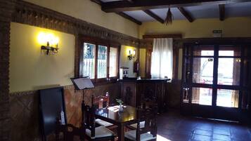A rustic interior with a wooden table, chairs, a music stand, and a door labeled "SALIDA".