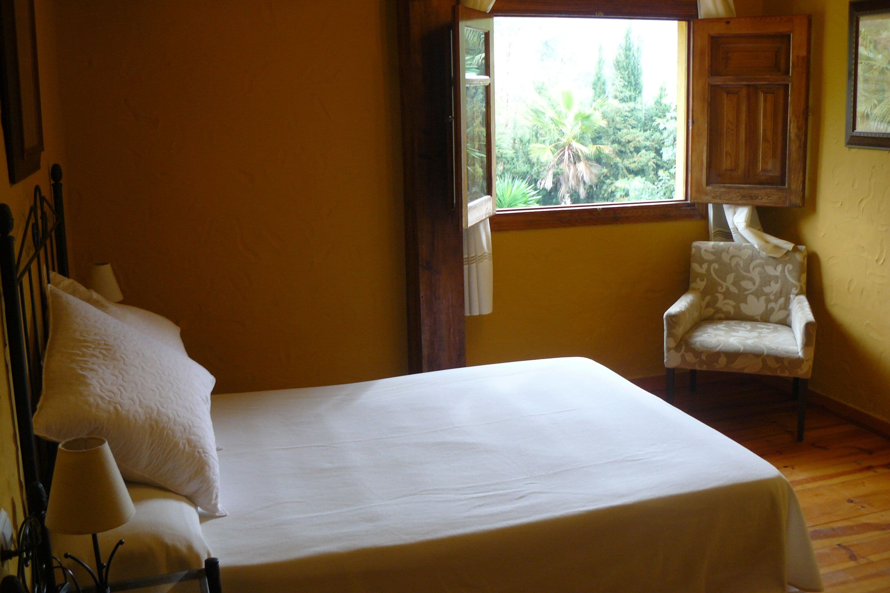 Ein Zimmer mit einem Bett, einem Sessel und einem Fenster mit Blick auf Grünflächen.