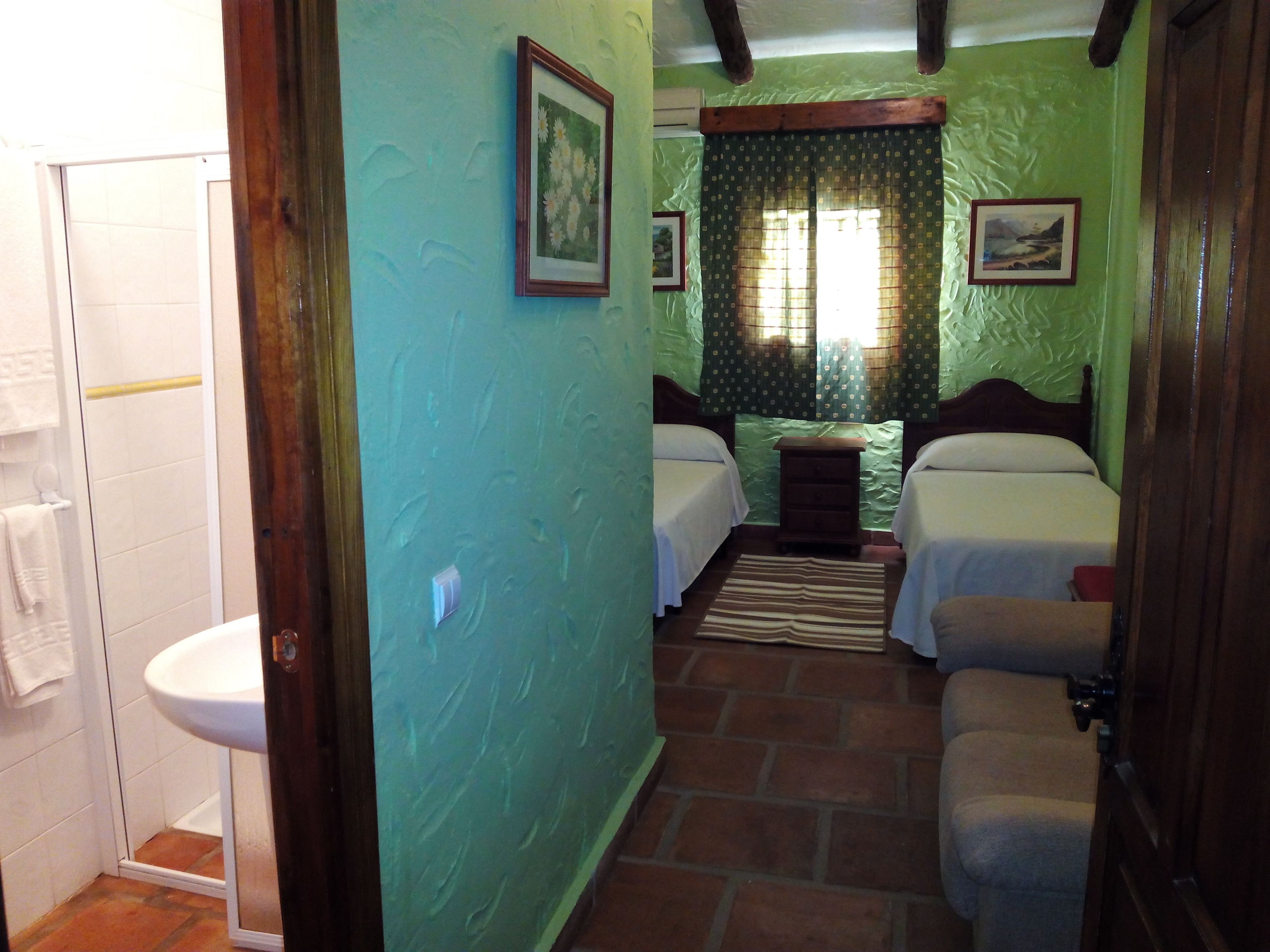 Una habitación con dos camas, una mesita, un lavamanos y una ducha.