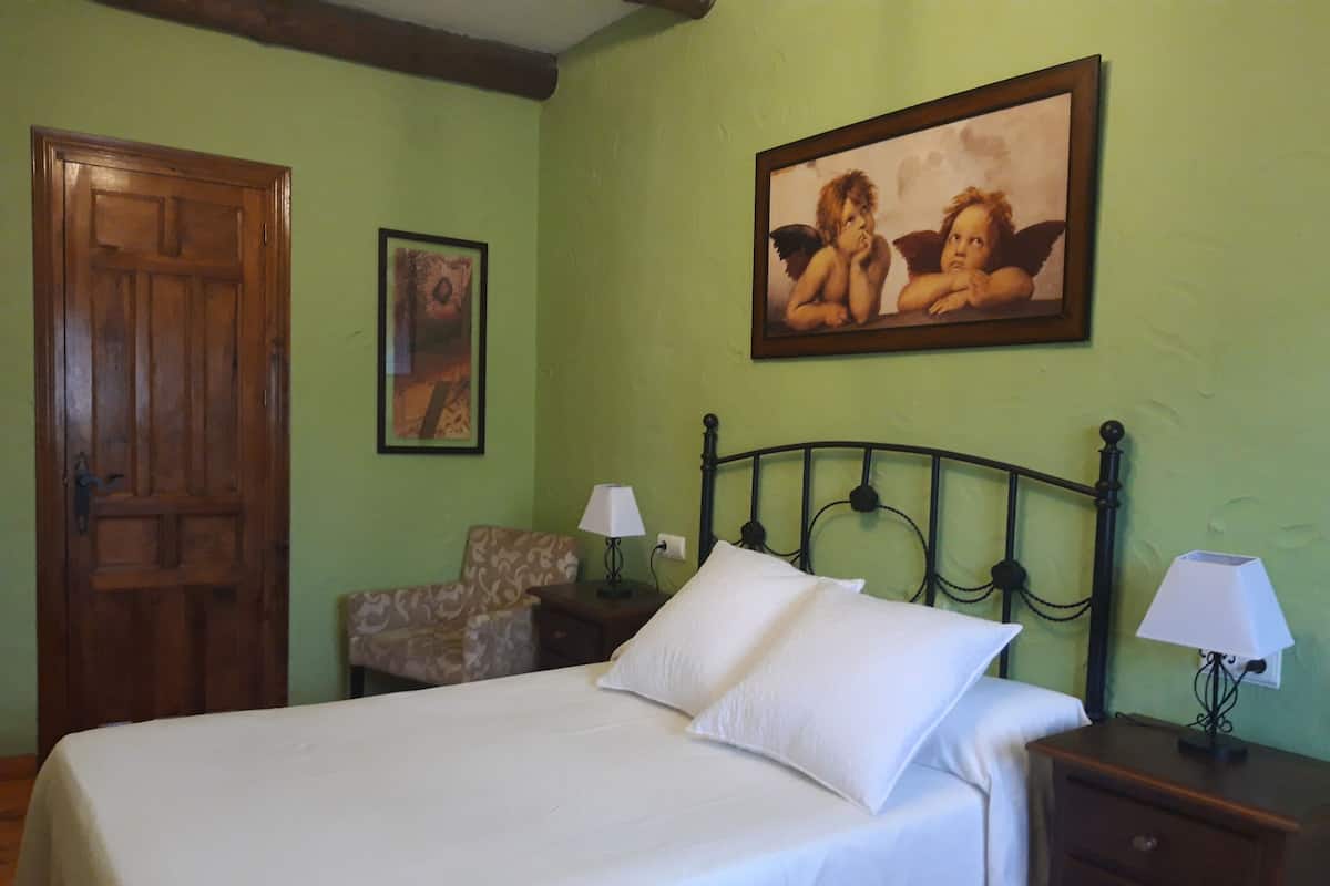 Ein Schlafzimmer mit einem Bett, zwei Nachttischen mit Lampen, einem Sessel, einer Holztür und einem gerahmten Bild an der Wand.