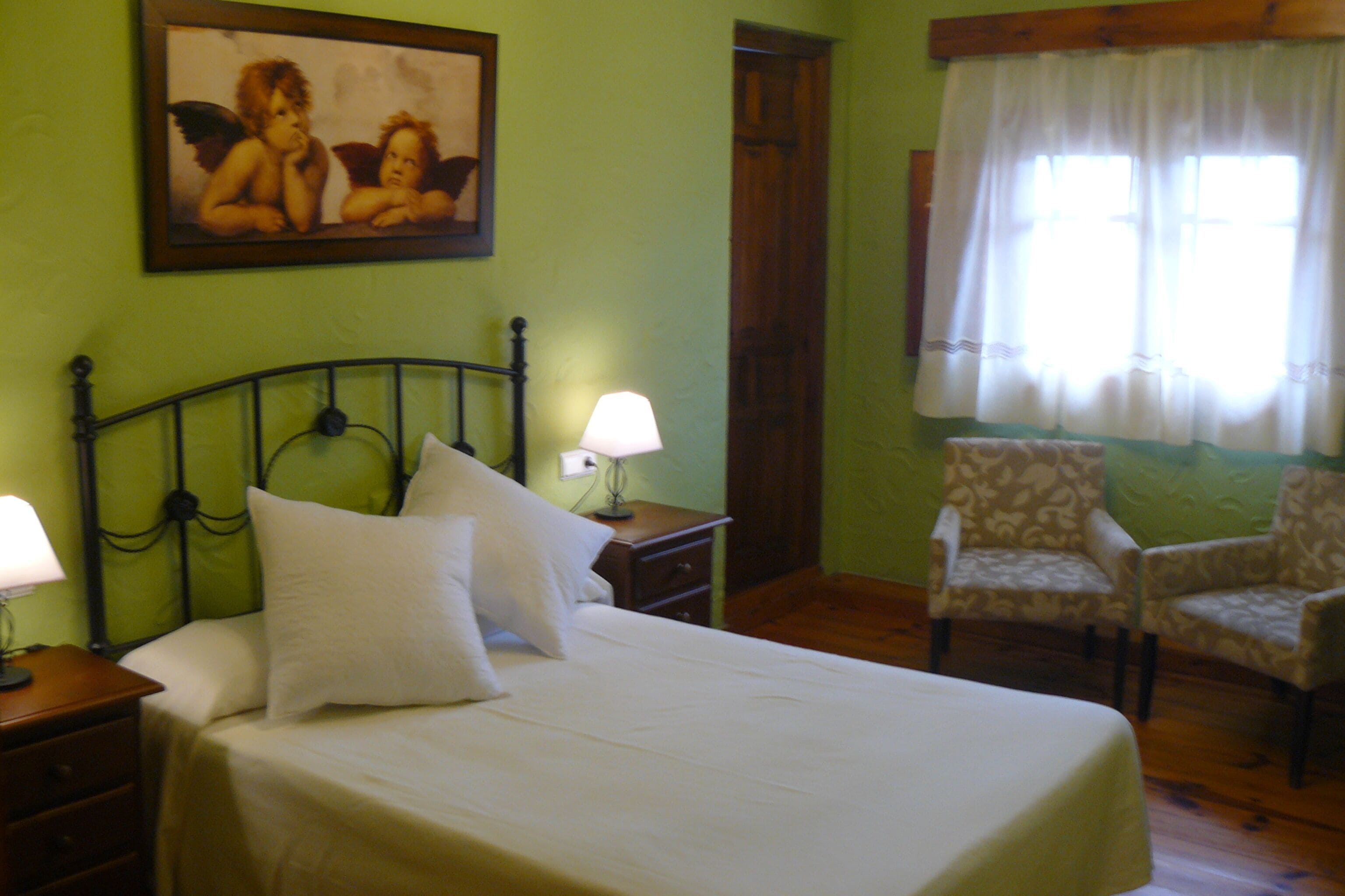 Une chambre à coucher avec un lit, deux tables de chevet avec des lampes, une chaise, une porte et un tableau au mur.