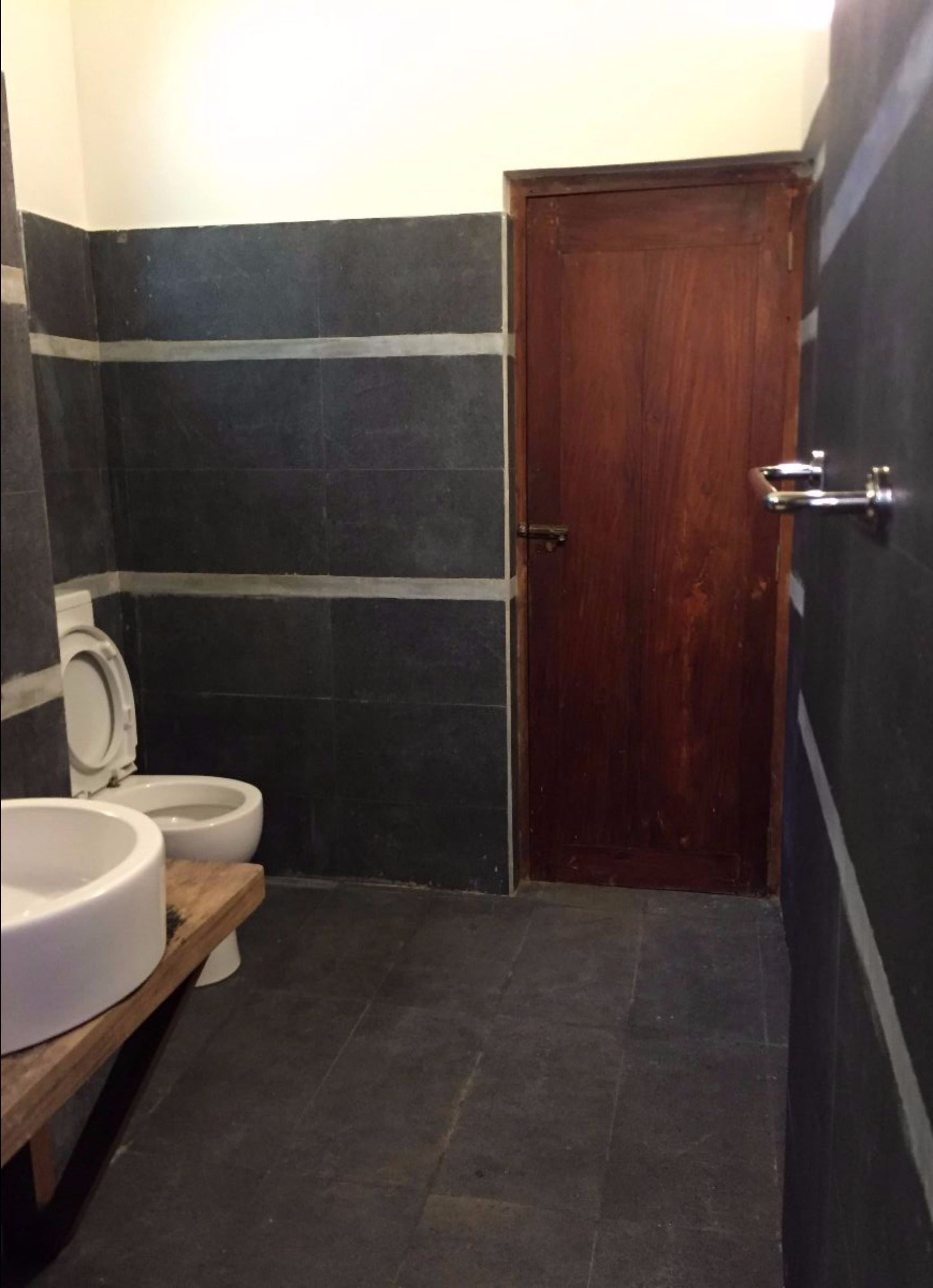 A small bathroom with a wooden door, a white toilet, and a wooden vanity with a white sink.