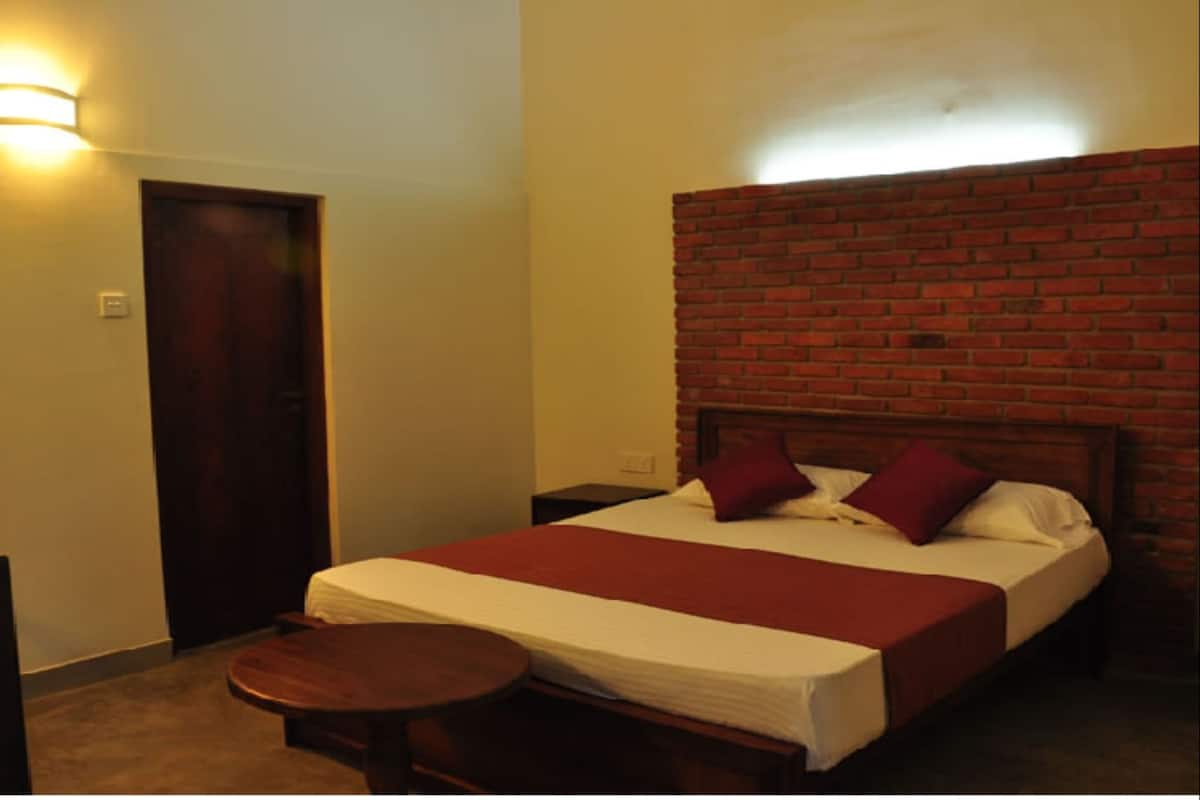 A hotel room with a brick headboard, a wooden bed frame, a small round table, and a door.