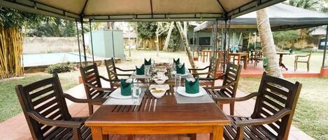 An outdoor dining area with a covered table and chairs, surrounded by a garden view.