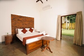 A bedroom with a brick accent wall, a wooden bed frame, a bedside table, and a small round table. - Gedara Resort (Wadduwa)