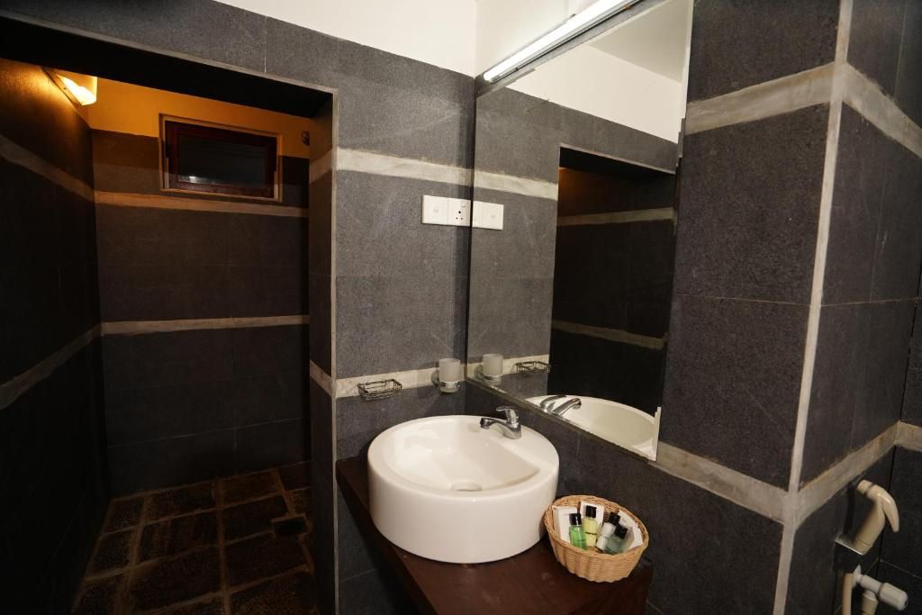 Un bagno con un lavandino bianco, uno specchio e una parete rivestita di piastrelle scure.