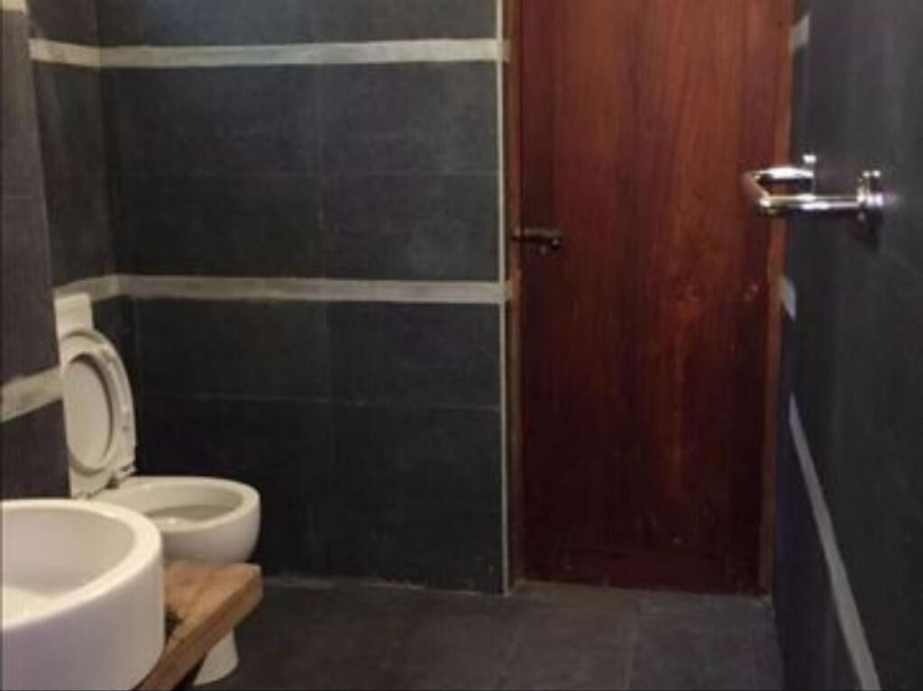 Un baño con dos inodoros, paredes de azulejos oscuros y una puerta de madera.