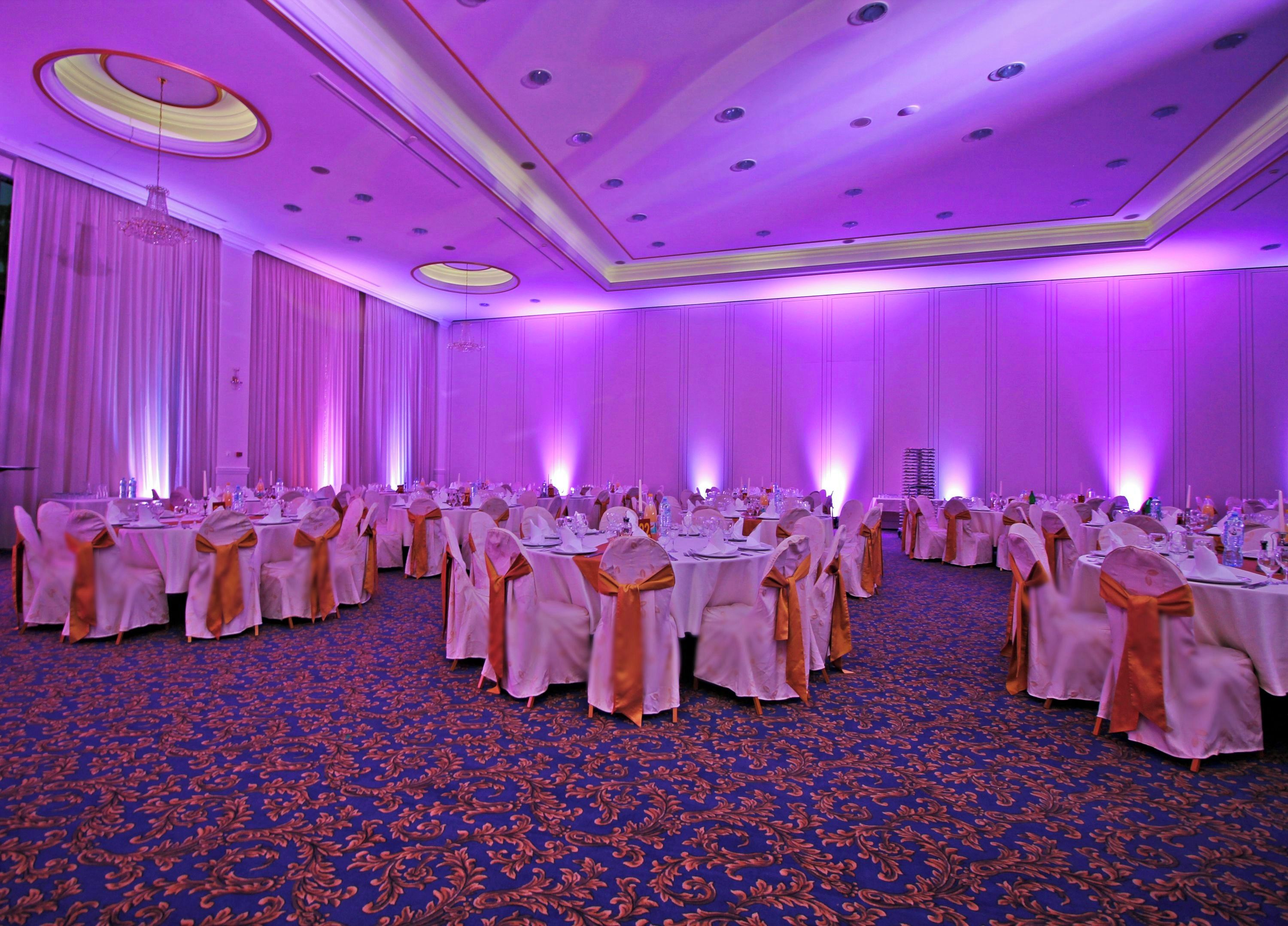 Un salón de banquetes con mesas redondas, sillas y una alfombra azul estampada.