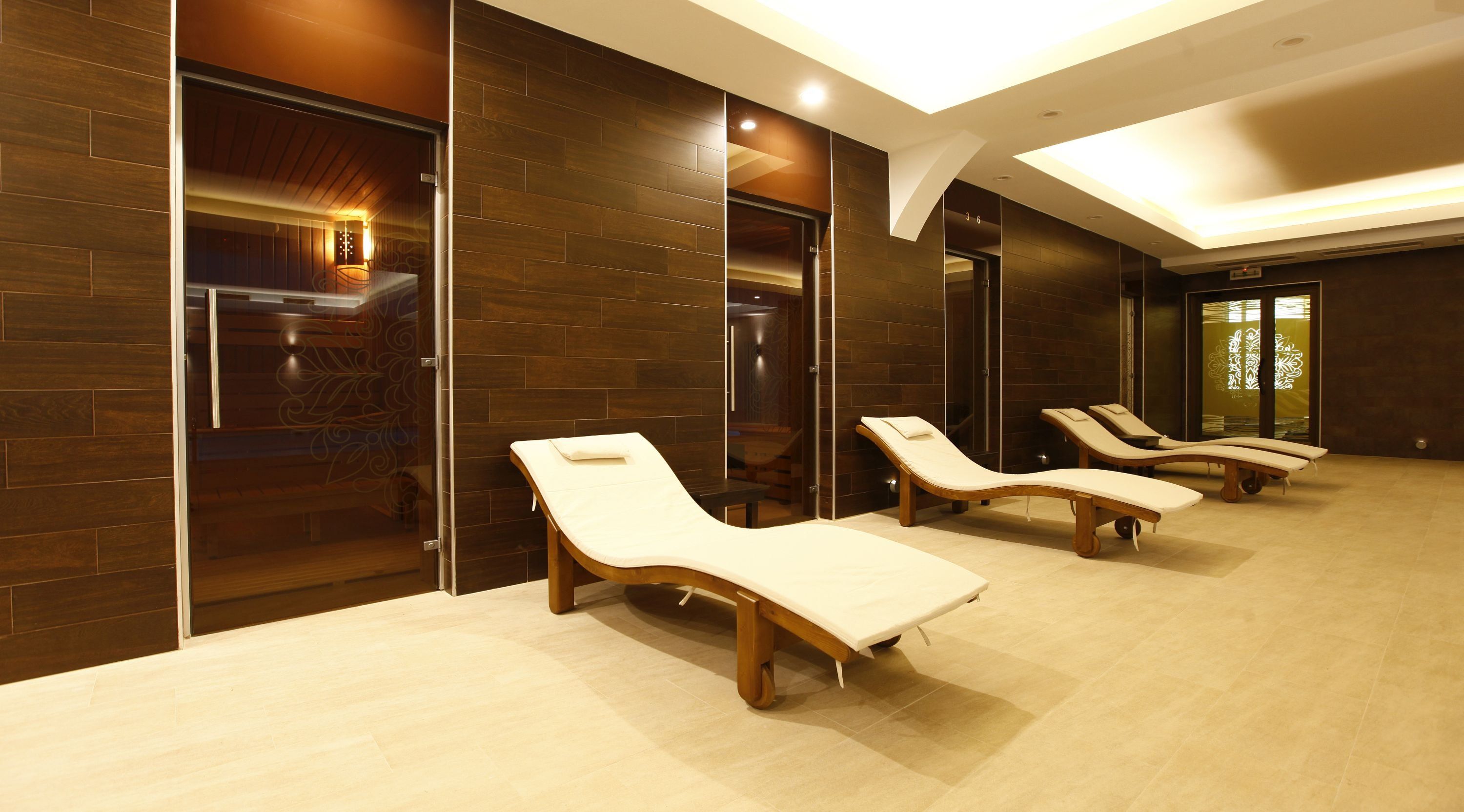 A spa room with wooden walls, a massage table, and three sun loungers.