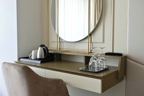 A hotel room with a desk, a chair, a mirror, a kettle, a cup, a remote control, and wine glasses. - Aleksander Palace (Skopje)