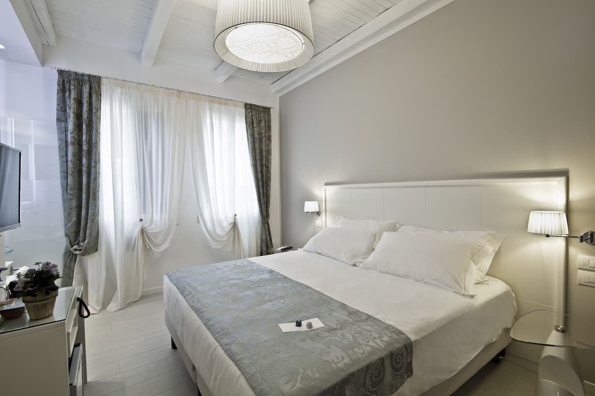 A hotel room with a bed, bedside lamps, a TV, and a desk with a lamp.