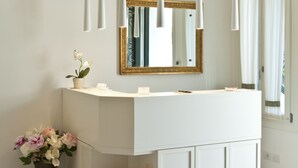 Um banheiro moderno com um lavatório branco, luminárias pendentes, um espelho e um vaso com flores.