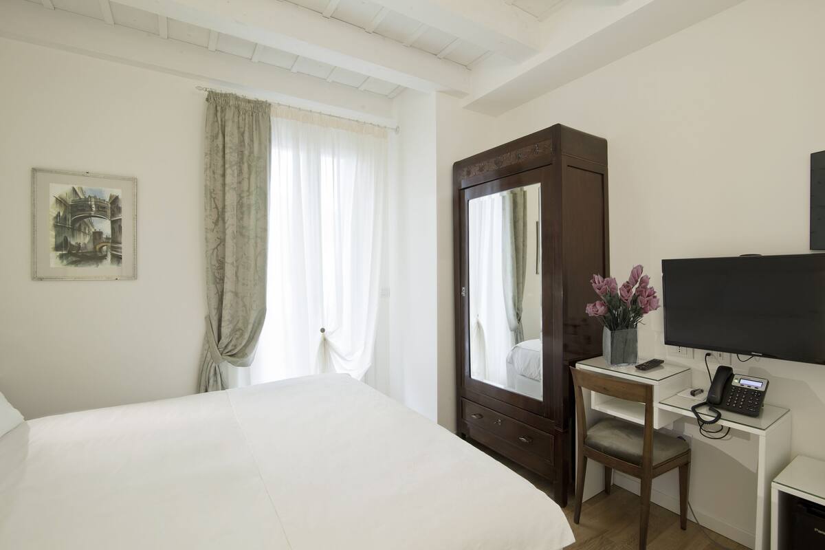 A hotel room with a large bed, a desk with a telephone, a mirror, and a painting on the wall.