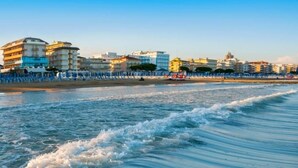 Um hotel à beira-mar com vários andares, uma praia arenosa e céu claro.
