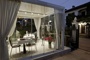 A glass-enclosed dining area with a table and chairs, a vase with flowers, and a view of the street. - Chiara Lodge (Mestre)