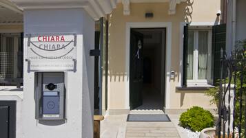 Entrada de hotel con un letrero que dice "CHIARA CHIARA YOUR COMFORTABLE LODGE" y una cámara de seguridad.