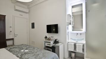 A hotel room with a bed, a desk with a telephone, a television, a bathroom with a sink and mirror, and a trash can.