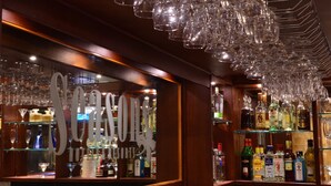 Zona de bar con una variedad de botellas de licor y vasos exhibidos en estanterías.