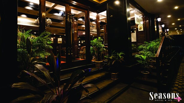 Entrada de un hotel con suelo a cuadros, plantas en macetas y una escalera que conduce al interior.