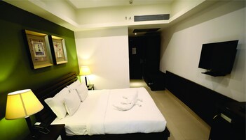 Una habitación de hotel con cama, lámparas de noche, televisor de pantalla plana y un cuadro en la pared.